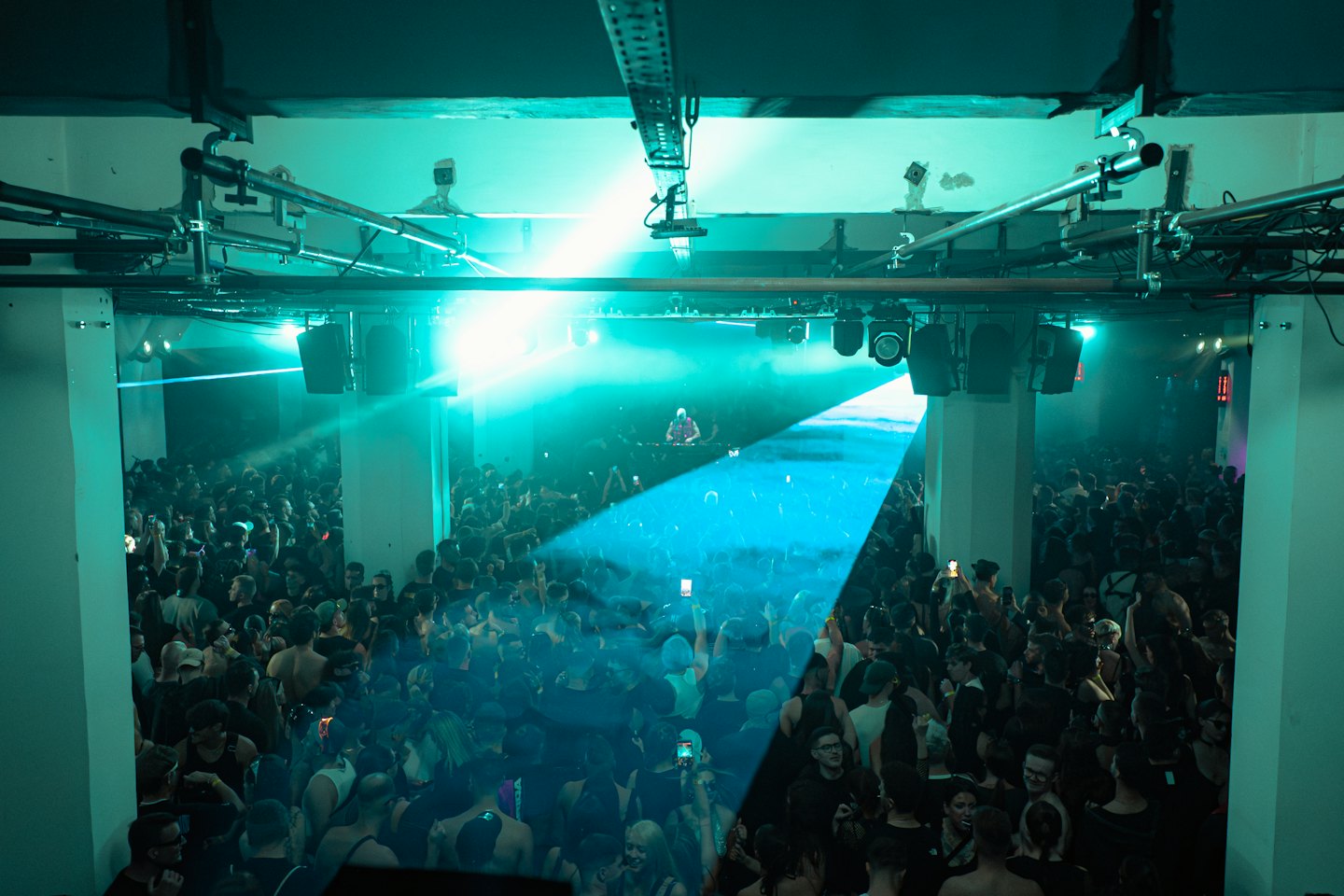 Crowd dancing at a nightclub while a DJ performs onstage.