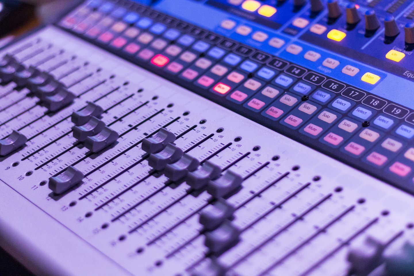 Audio mixing console with many faders and glowing buttons.